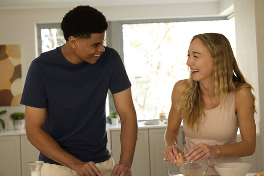 Couple laughing while cracking egg into clear mixing bowl at home kitchen, navy T-shirt, beige top