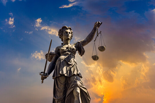 historic statue of lady justice - Justitia - in Frankfurt with scale and sword at sunset with dramatic sky.