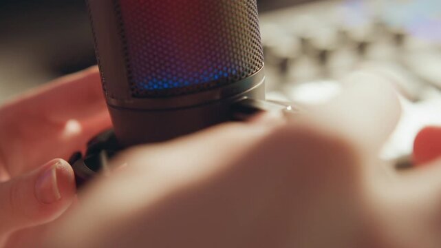 Close-up shows large-diaphragm condenser microphone secured in shock mount while hands tighten mounting clamp and refine position, with slight motion blur and warm studio lighting, with microphone