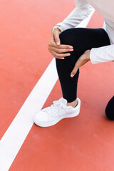 Fototapeta premium Close-up of an Asian woman holding her painful knee on running track during workout. Knee injury, joint pain, runner's knee, sports accident, and healthcare concept. Vertical Shot