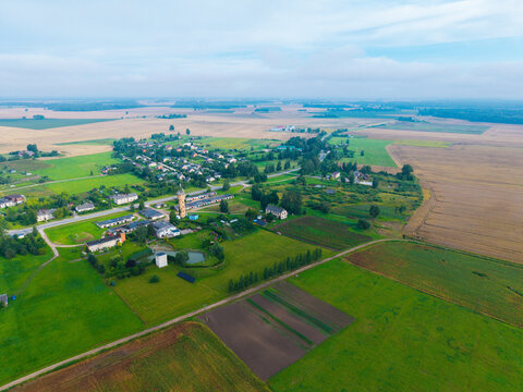 Aerial view of the rural village of Jaunberze featuring a historic water tower, surrounding agricultural fields, and green meadows in Jaunberze, Dobele Municipality, Latvia.
