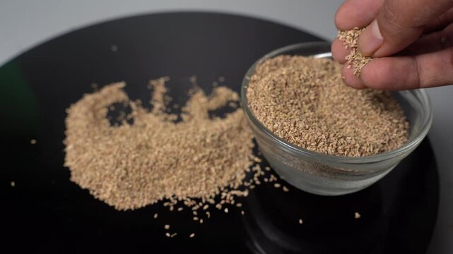 Close-up View of a Hand Holding and Sprinkle Carom Seeds, known as Ajwain, onto a Black Surface