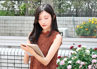 タブレット端末を持ち画面を操作する若い女性 © taka