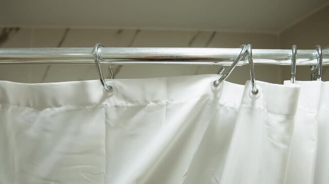 White shower curtain secured to chrome rod with metal rings, fabric gathered into vertical folds with embossed floral texture, soft sheen, and gentle movement inside tiled bathroom