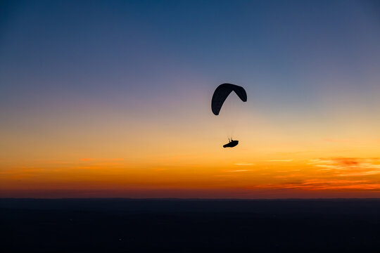 Paraglider silhouetted against a spectacular sunset, representing freedom, adventure and escape. Atmospheric image for travel, outdoor lifestyle, tourism and the dream of flying.
