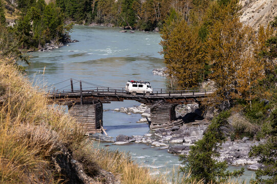 UAZ offroad van crossing old wooden bridge over dangerous Argut river in Altai. 4x4 expedition on remote mountain road near Arkyt village. Extreme rafting and kayaking travel destination, Russia