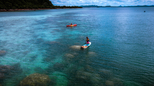 Top aerial view of Group of tourist are enjoy on water sport paddle sup-board with kayaking along at the edge of the sea beach under crystal clear of water in the island of summer trip
