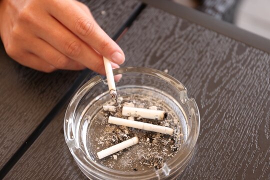 Woman flicking ash from cigarette into ashtray at wooden table, closeup
