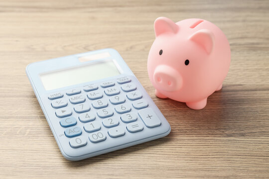 Piggy bank and calculator on wooden table, closeup