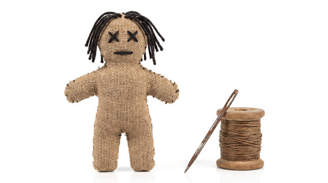 Handmade burlap voodoo doll standing beside a large needle and wooden spool of thread on a white background for cultural articles, horror book covers, and seasonal marketing campaigns.