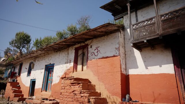 Row of weathered traditional mud and stone houses with sacred red om symbol painted on whitewashed wall beside a rustic stone staircase in Nepal