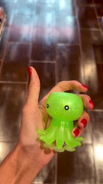 Female hand squeezing a shiny green octopus squishy toy. Vertical 4K close-up video showcasing tactile sensory play, stress relief, satisfying texture, relaxation and colorful fidget toy concept