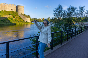 Fototapeta premium Woman with headphones dancing on riverside walkway near fortress
