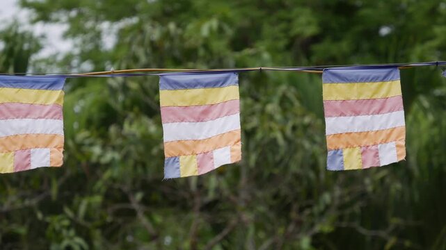 Colorful buddhist prayer flags waving on a line in the wind with green foliage behind. Cultural tradition.