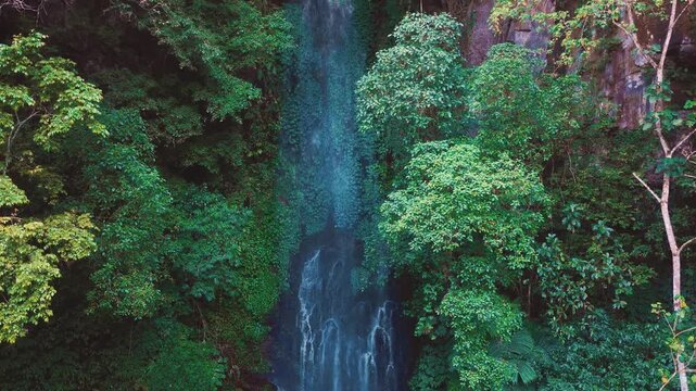Aerial drone view of Coban Kaca waterfall flowing through dense tropical forest in Malang, East Java, Indonesia. The narrow waterfall cascades between lush green trees. 