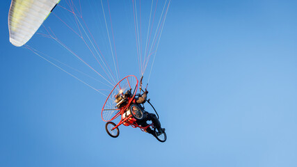 Powered paraglider with red wheeled trike flying high in the clear blue sky, extreme aviation stock photo. © Dmytro