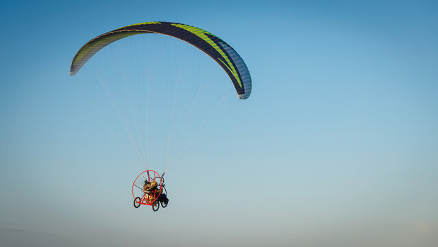 Powered paraglider with a trike flies high in the clear blue sky, capturing a moment of extreme sport and extreme freedom.
