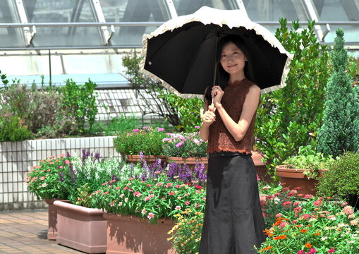 花壇のある屋外テラスで日傘をさして微笑む若い女性