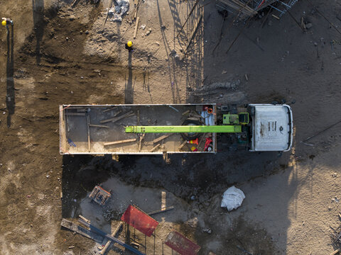 Aerial view of the Construction of the Solo-Yogyakarta Toll Road with a crane truck and workers on a dusty site in Kecamatan Depok, Daerah Istimewa Yogya, Indonesia.