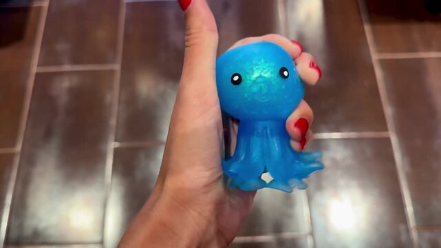 Female hand squeezing a shiny blue octopus squishy toy. Horizontal 4K close-up video showcasing tactile sensory play, stress relief, satisfying texture, relaxation and colorful fidget toy concept