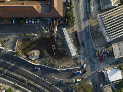 Aerial view of the Solo-Yogyakarta Toll Road construction with heavy machinery and concrete structures near a busy intersection in Kecamatan Depok, Daerah Istimewa Yogya, Indonesia.