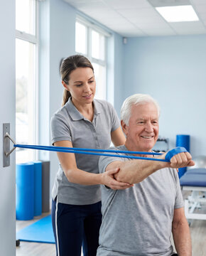 Physical therapist guiding a seated senior patient through a resistance-band shoulder exercise