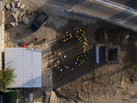 Aerial view of construction of the Solo-Yogyakarta Toll Road with workers in yellow hard hats on the dirt site near a metal structure in Kecamatan Depok, Daerah Istimewa Yogya, Indonesia.