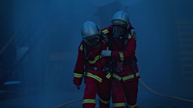 Firefighters in full protective gear are helping an injured colleague out of a burning building for first aid during a fire safety drill