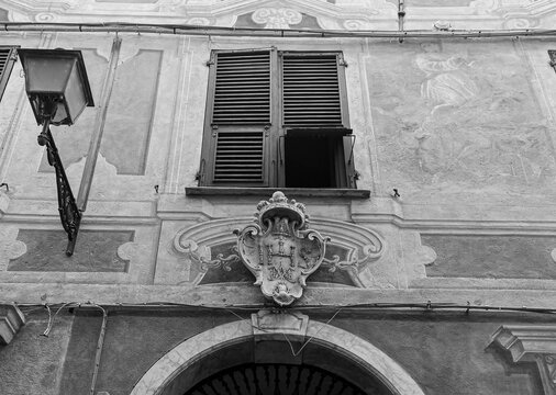 Black and white low angle view of an ancient IHS christogram monogram above an entrance window in the historic Budello alley of Alassio, Liguria, Italy