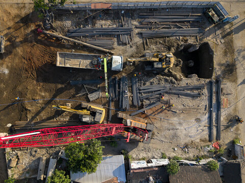 Aerial view of the Solo-Yogyakarta Toll Road construction site featuring heavy machinery, excavators, a crane, and steel reinforcement bars in Kecamatan Depok, Daerah Istimewa Yogya, Indonesia.