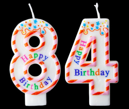 Number eighty four shaped birthday candle with colorful sprinkles and Happy Birthday text isolated on a black background