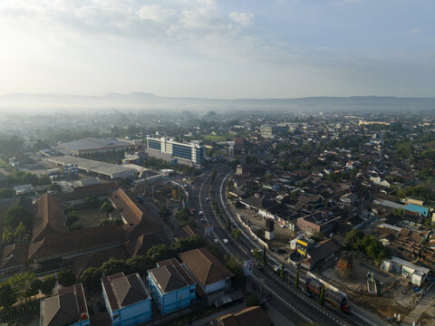 Aerial view of INNSiDE by Melia Yogyakarta hotel surrounded by urban sprawl, roads, and misty morning light in Kecamatan Depok, Daerah Istimewa Yogya, Indonesia.
