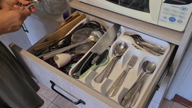 Organizing kitchen utensils in a drawer at home during the afternoon