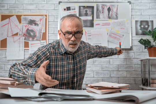 Agitated older man gesturing toward a conspiracy board while explaining his theory with a shocked and suspicious expression.