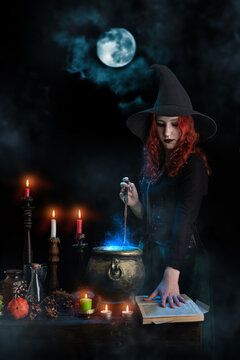 Witch with magic wand casts spell, cauldron, boiling magic potion, candles. Woman learns witchcraft from a book, magician girl with red hair, dressed in Halloween attire and conical hat