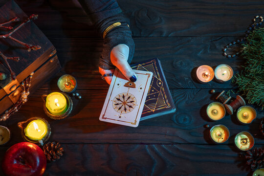 A witch fortune teller casts a spell on Tarot cards among candles and pumpkins. A sorceress on Halloween night.