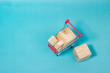 Top view of a red miniature shopping cart carrying blank wooden block packages on a solid turquoise background surface. High Quality Photo © 7TridentSea