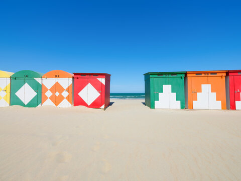 Colorful beach huts on a sandy shore by the sea under a clear blue sky. Summer vacation and travel landscape.