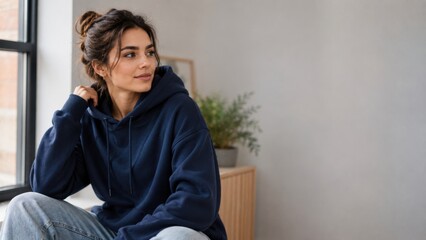 Obraz premium Young Woman Wearing Navy Blue Hoodie Relaxing Indoors by Window with Cozy Lifestyle Mood and Copy Space