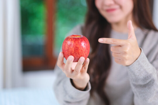 Closeup image of a woman holding and pointing finger at a red apple