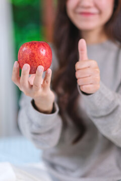 Vertical closeup image of a woman showing thumbs up hand sign while holding a red apple