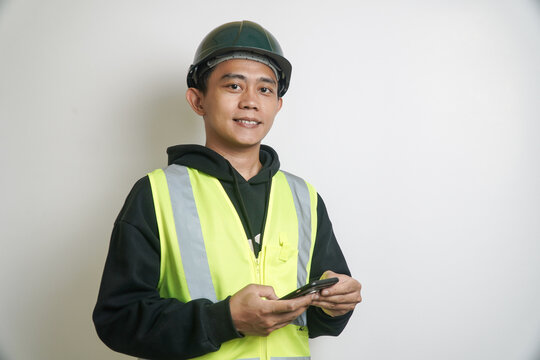 Smiling Young Construction Worker in Safety Vest and Hard Hat Using Smartphone