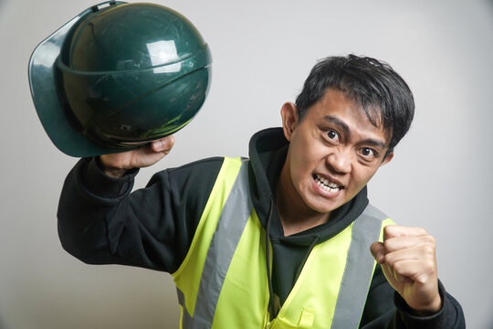 Furious Asian Man in Safety Vest Gripping Hard Hat and Clenching Fist