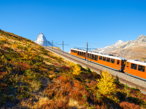 Passenger train on a railway in Zermatt, Switzerland. Autumn nature in the Alps. Train passes through autumn forest with Matterhorn peak in background.