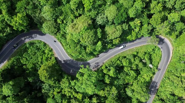 Aerial view of two cars traveling in opposite directions along a winding mountain road. The location is in Sumatra, Indonesia.