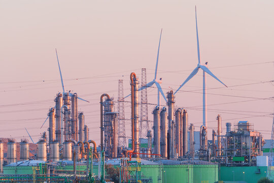 Industrial pipes and equipment at an oil refinery plant with wind turbines in the background. Petroleum production and renewable energy infrastructure.