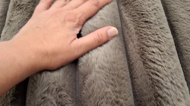A hand gently touches plush beige fabric in a textile store, soft material, tactile shopping experience, cozy home design, interior comfort.