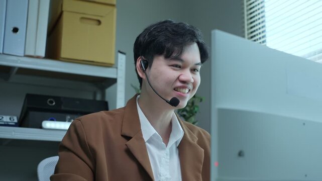 Asian male telesales and customer support representative talking with headset in office
