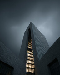 Fototapeta premium Modern glass skyscraper viewed from a low angle under a dark overcast storm sky