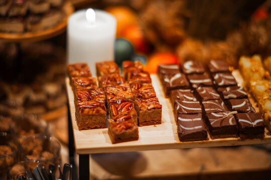 Artisan pecan blondies and rich chocolate brownies with white icing swirls arranged on a wooden serving tray at a warmly lit craft food market